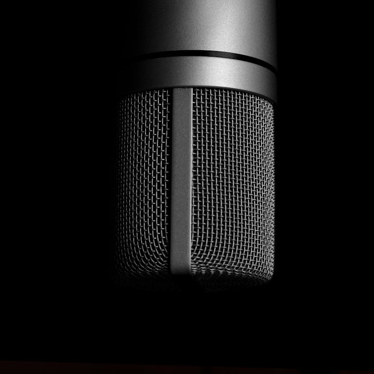 Detailed close-up shot of a metallic studio microphone on a black background, emphasizing sound recording equipment.